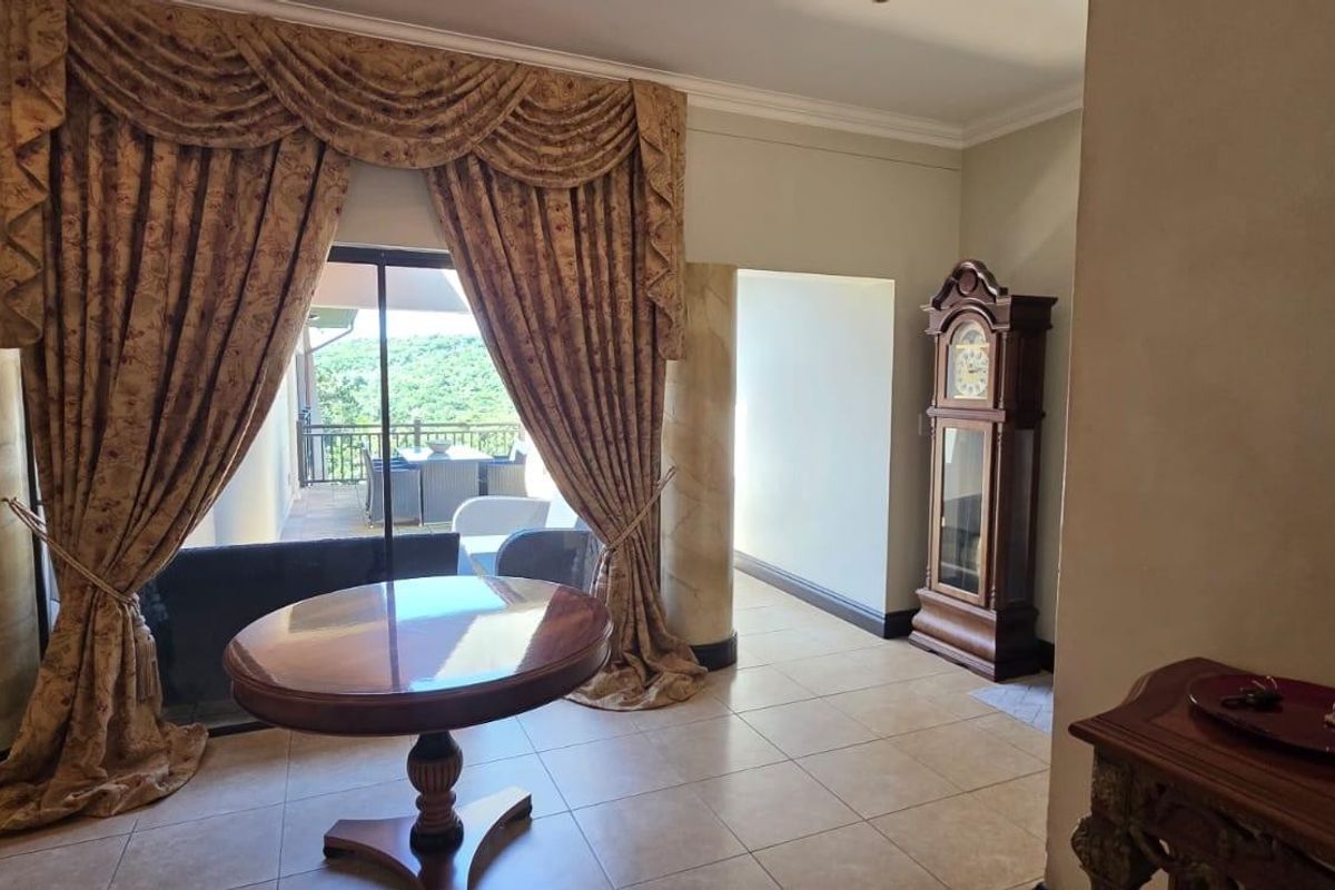 A living area featuring tiled flooring, decorative columns, and a large sliding glass door providing access to an outdoor patio.
