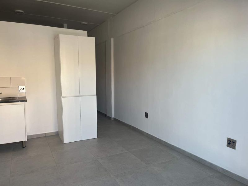A minimalist, empty kitchen area featuring modern grey floor tiles, white built-in cabinetry, and a compact sink unit.