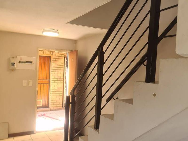 A functional hallway featuring a staircase with a metal balustrade, tiled flooring, and an accessible electrical distribution board near the entrance.