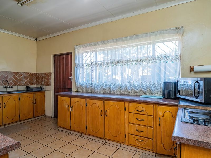 A functional kitchen featuring wooden cabinetry, laminate countertops, a built-in electric hob, and tiled flooring, offering potential for a modern renovation.