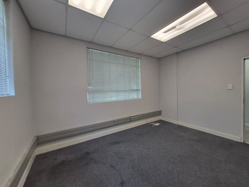 A clean, empty office space featuring a suspended ceiling with recessed lighting, carpeted flooring, and perimeter trunking for electrical and data cabling.
