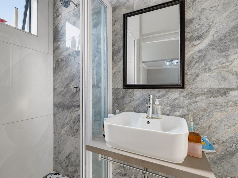 Modern bathroom featuring a vessel sink, chrome faucet, and a glass-enclosed shower with stylish marble-effect wall tiling.