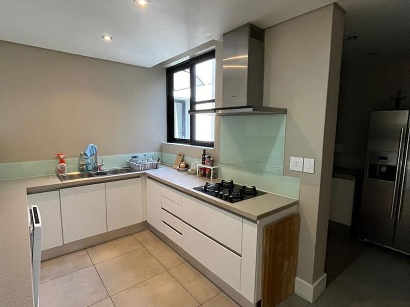 Modern kitchen featuring white cabinetry, stone countertops, a gas hob with extractor fan, glass splashback, and neutral tiled flooring.