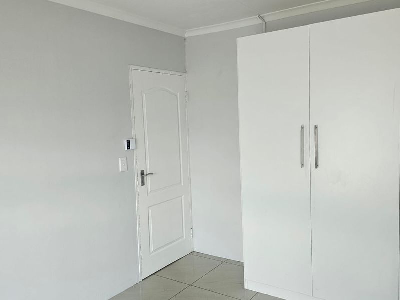 A clean, neutral bedroom featuring tiled flooring and a built-in white wardrobe, offering a blank canvas for personalization.