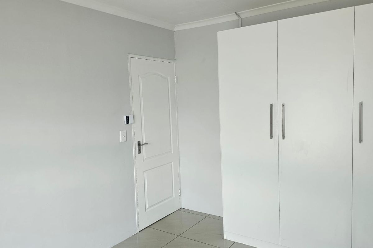 A clean, neutral bedroom featuring tiled flooring and a built-in white wardrobe, offering a blank canvas for personalization.