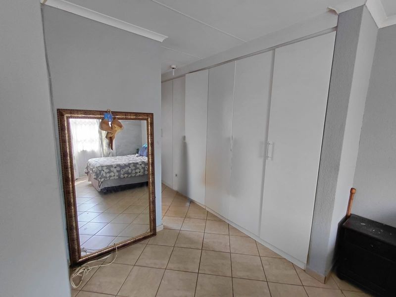 Bedroom featuring tiled flooring and extensive white built-in cupboards, offering ample storage space within a neutral interior setting.