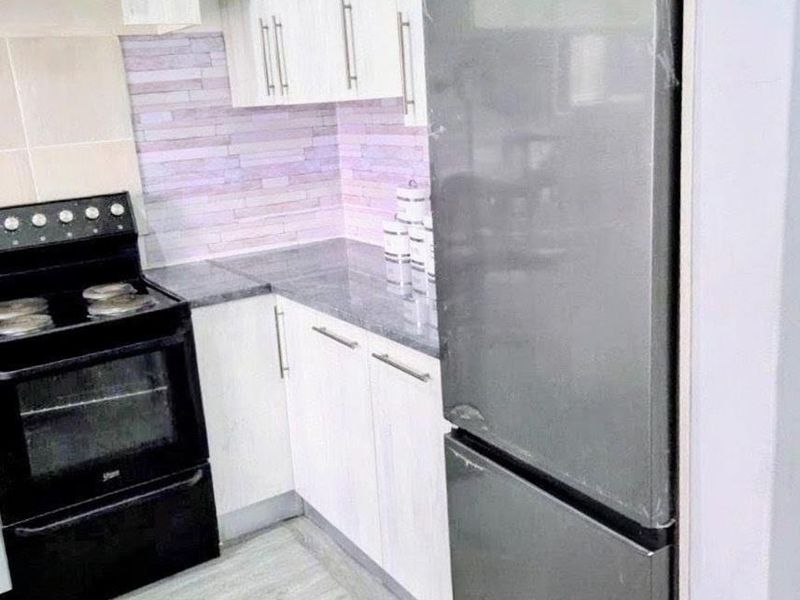 A compact, modern kitchen featuring white cabinetry, grey laminate countertops, a tiled backsplash, and light-toned laminate flooring.