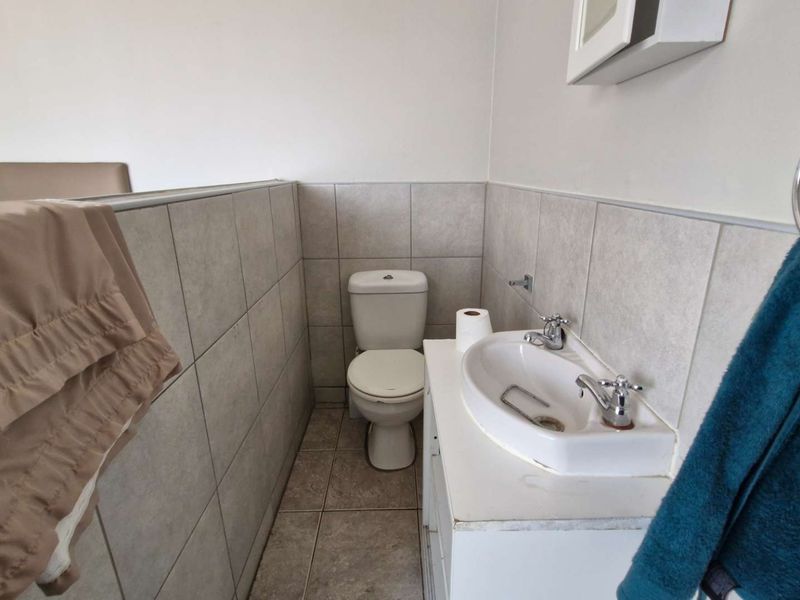 A functional bathroom featuring a toilet, vanity with basin, and neutral wall and floor tiling.