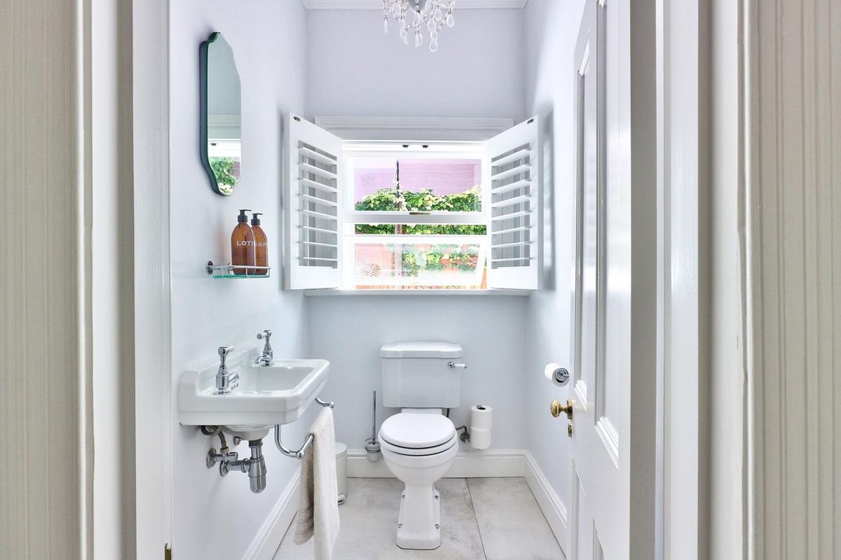 A bright and well-maintained bathroom featuring a wall-mounted basin, toilet, and elegant plantation shutters, finished with clean tiled flooring.