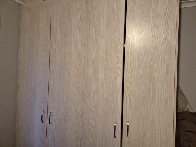 A bedroom featuring light wood-grain finish built-in wardrobes with modern metal handles.