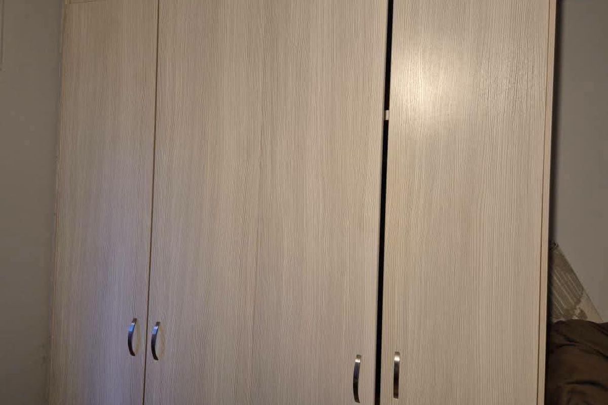 A bedroom featuring light wood-grain finish built-in wardrobes with modern metal handles.
