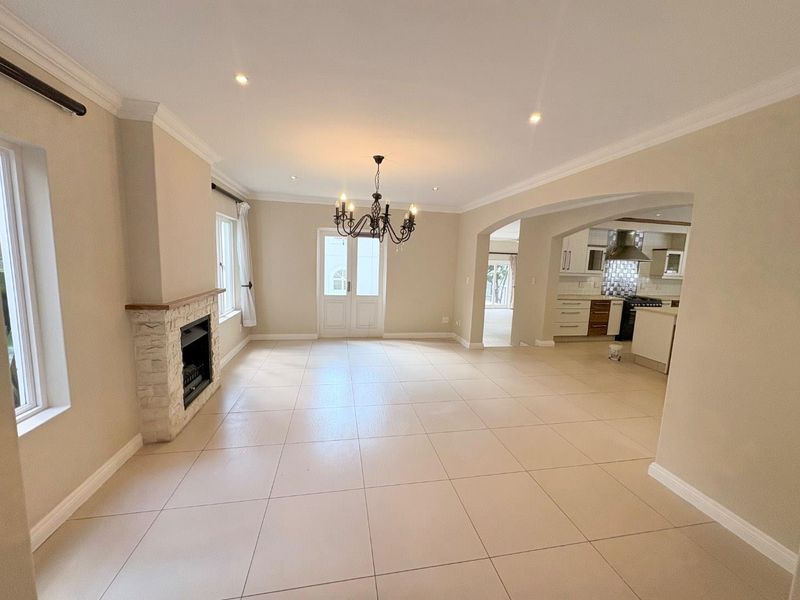 Spacious open-plan living and dining area featuring a stone fireplace, neutral tiled flooring, and seamless flow into the adjacent kitchen.