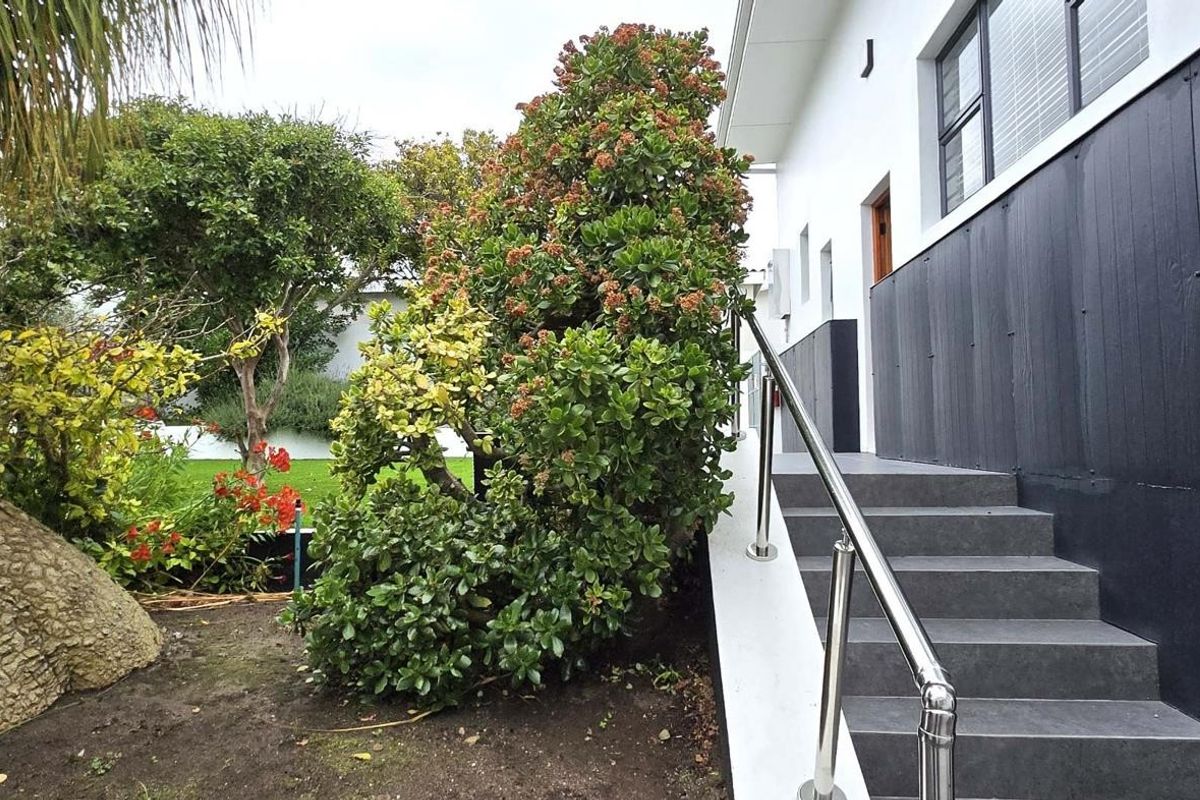 Exterior view of the property featuring a modern staircase with stainless steel handrails leading to the side entrance, adjacent to a landscaped garden area.