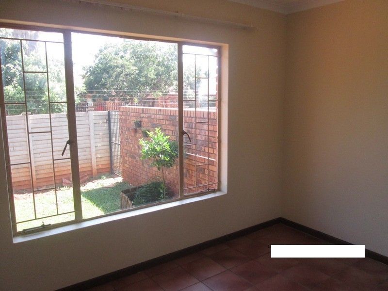 An empty bedroom featuring tiled flooring and large windows with security bars, offering a view of the rear garden area.