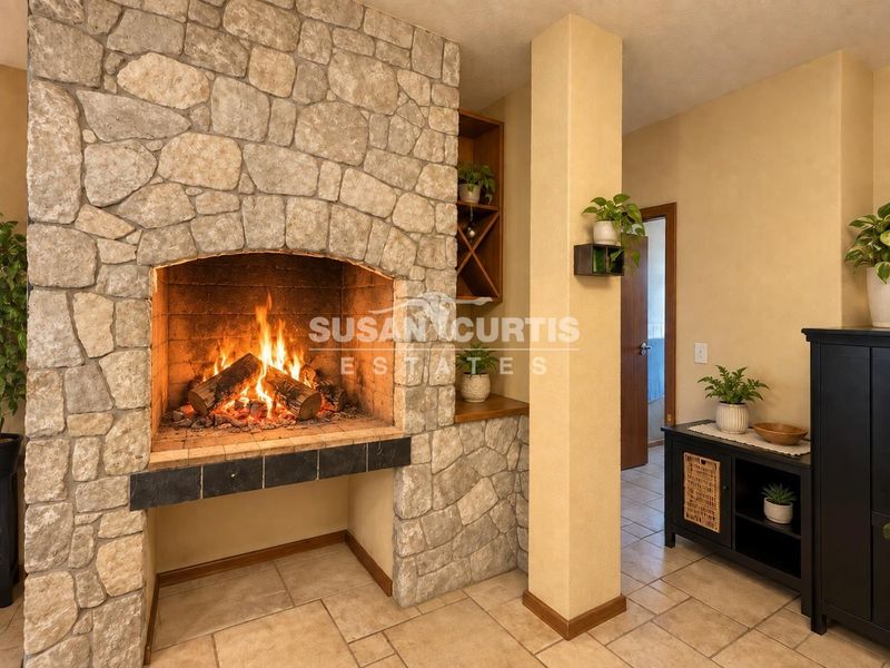A cozy living area featuring a prominent stone fireplace with a built-in hearth and integrated shelving, complemented by neutral ceramic tile flooring.