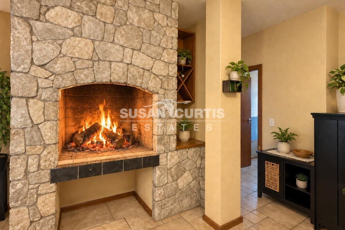 A cozy living area featuring a prominent stone fireplace with a built-in hearth and integrated shelving, complemented by neutral ceramic tile flooring.
