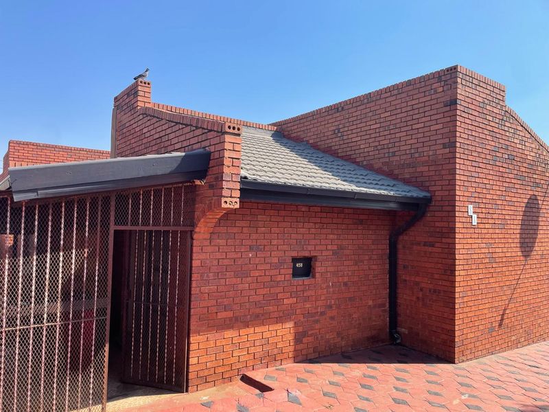 A view of the front facade featuring face brick construction, a tiled roof, and a secure gated entrance with paved driveway.