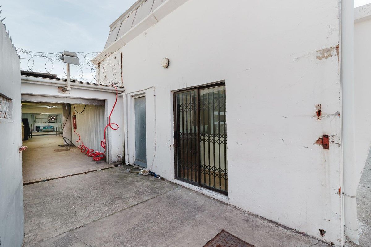 Rear exterior area featuring concrete paving, a security gate, and perimeter razor wire fencing, showing signs of wear and maintenance requirements.