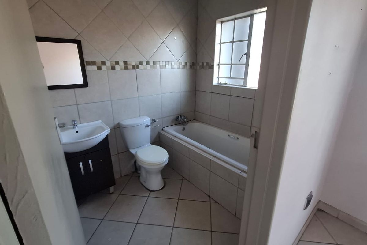 A functional bathroom featuring a vanity cabinet, toilet, and bathtub with tiled finishes, offering a blank canvas for potential modern updates.