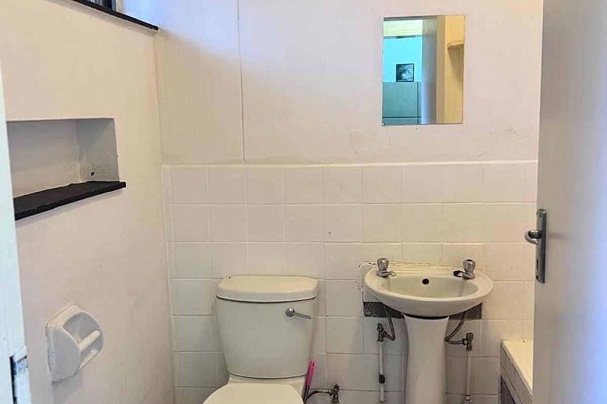 A compact bathroom featuring a pedestal sink, standard toilet, and tiled wall accents, requiring cosmetic updates to modernize the space.