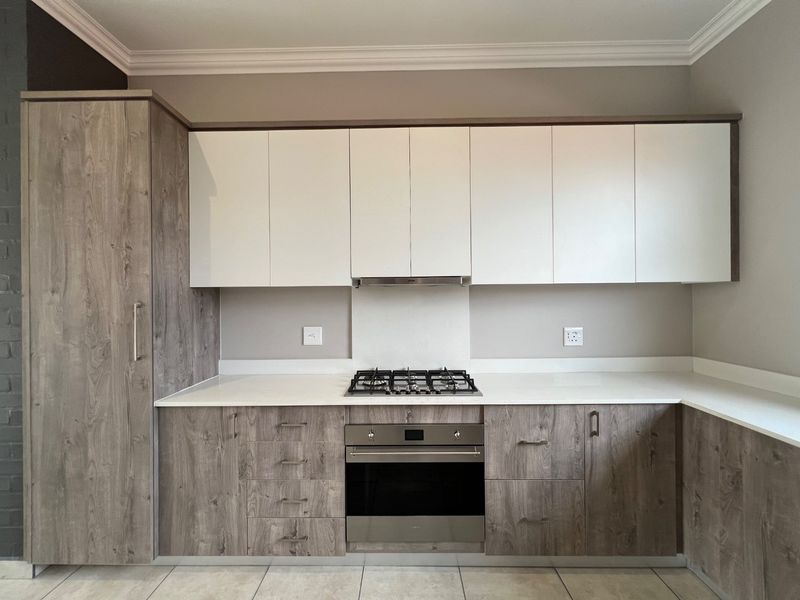 Modern kitchen featuring wood-grain and white cabinetry, stone countertops, a built-in gas hob, oven, and extractor fan with neutral tiled flooring.