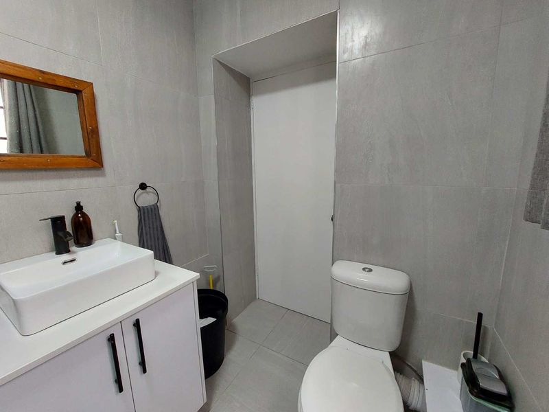 A modern bathroom featuring grey wall tiles, a white vanity cabinet with a vessel sink, and a standard toilet.