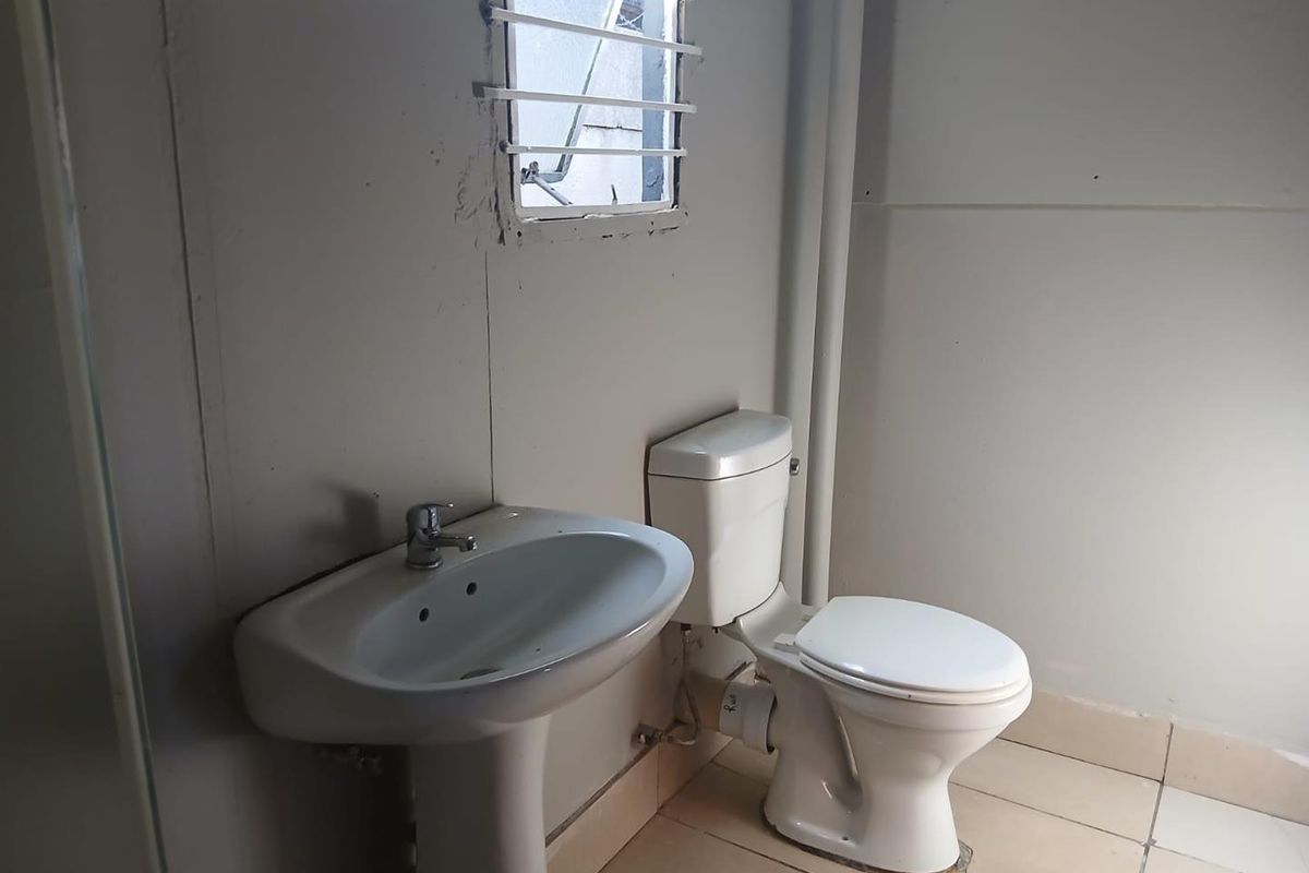 A functional bathroom featuring a pedestal basin and standard toilet, with visible plumbing and basic wall finishes.