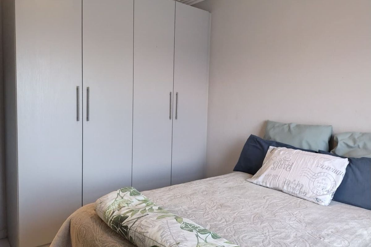A well-maintained bedroom featuring neutral walls and floor-to-ceiling built-in cupboards with modern handles.