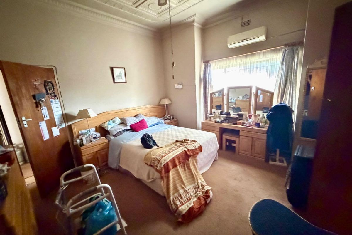 A spacious bedroom featuring a decorative pressed metal ceiling, wall-mounted air conditioning unit, and large window allowing for natural light.