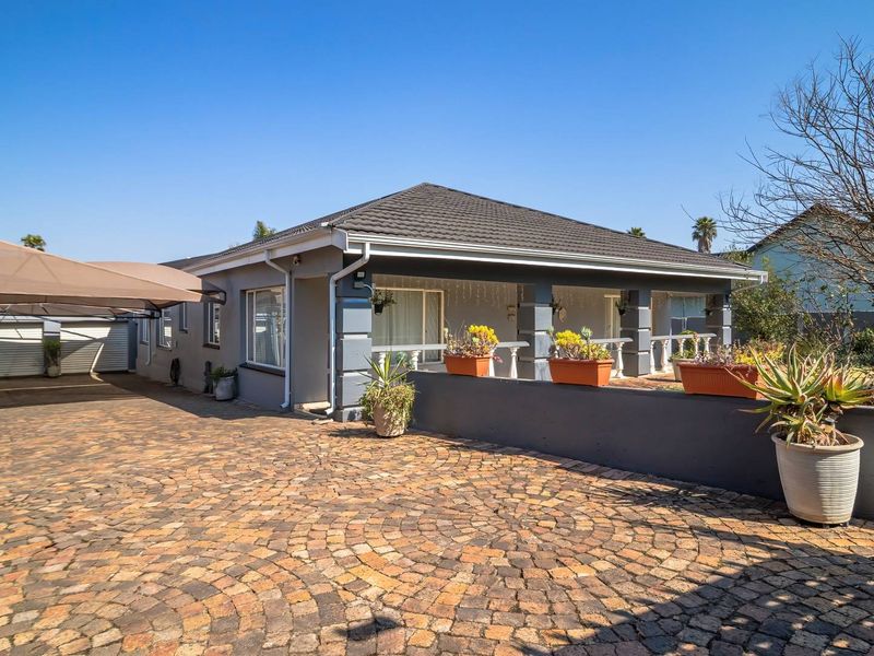 Front exterior view of the house featuring a paved cobblestone driveway, a covered carport, and a welcoming covered patio area.