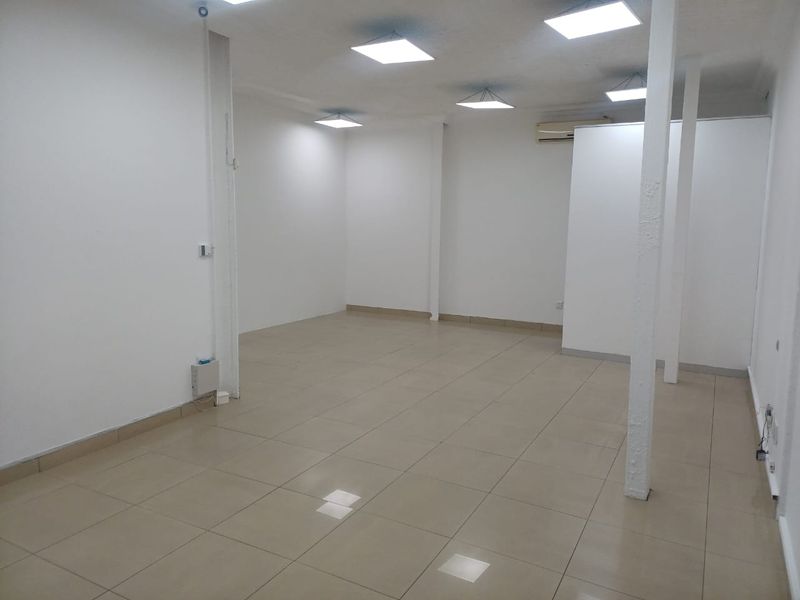 A spacious, vacant office area featuring neutral tiled flooring, recessed ceiling lighting, and a wall-mounted air conditioning unit, ready for custom fit-out.