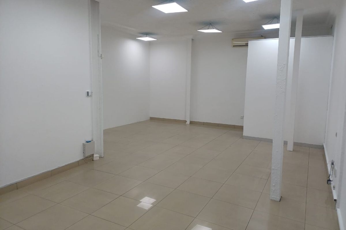 A spacious, vacant office area featuring neutral tiled flooring, recessed ceiling lighting, and a wall-mounted air conditioning unit, ready for custom fit-out.