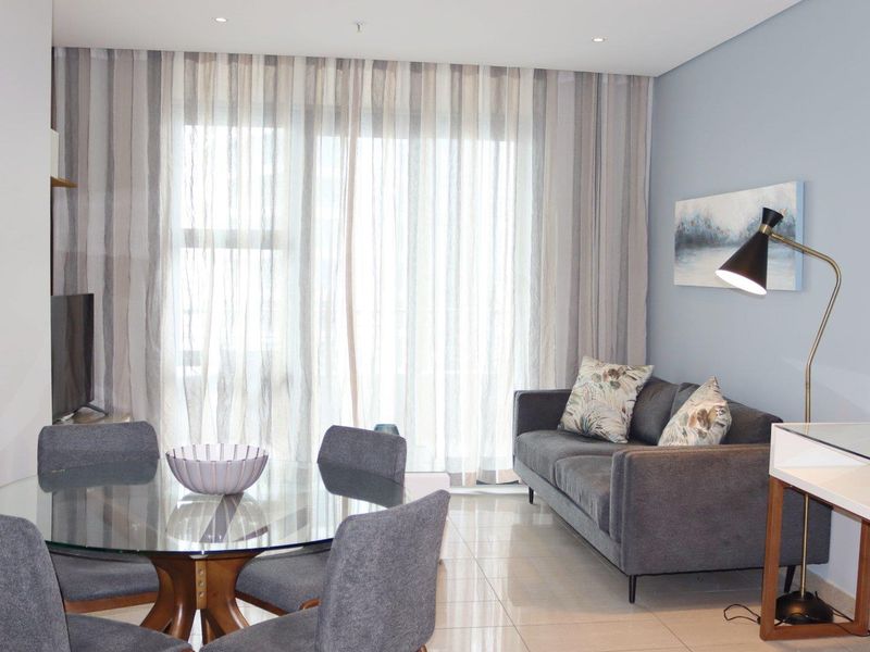 A bright and modern open-plan living and dining area featuring large sliding glass doors with floor-to-ceiling curtains and polished tile flooring.