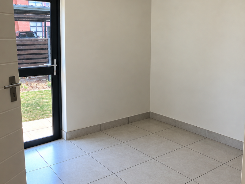 A bright, empty living area featuring neutral tiled flooring, clean walls, and a glass door providing direct access to the outdoor space.