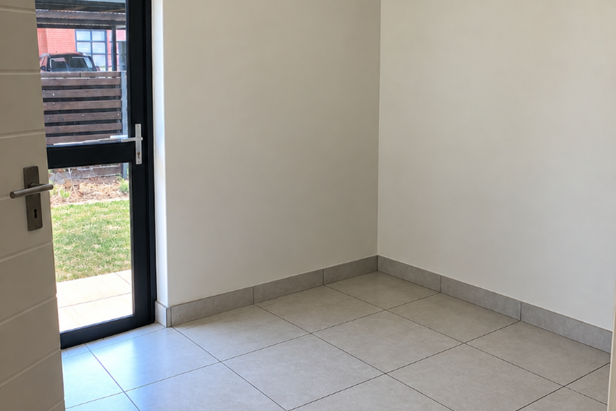A bright, empty living area featuring neutral tiled flooring, clean walls, and a glass door providing direct access to the outdoor space.