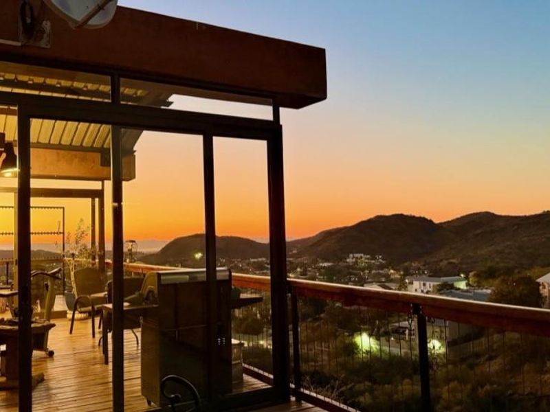 Elevated balcony featuring timber decking and sliding glass doors, offering expansive sunset views over the surrounding landscape.