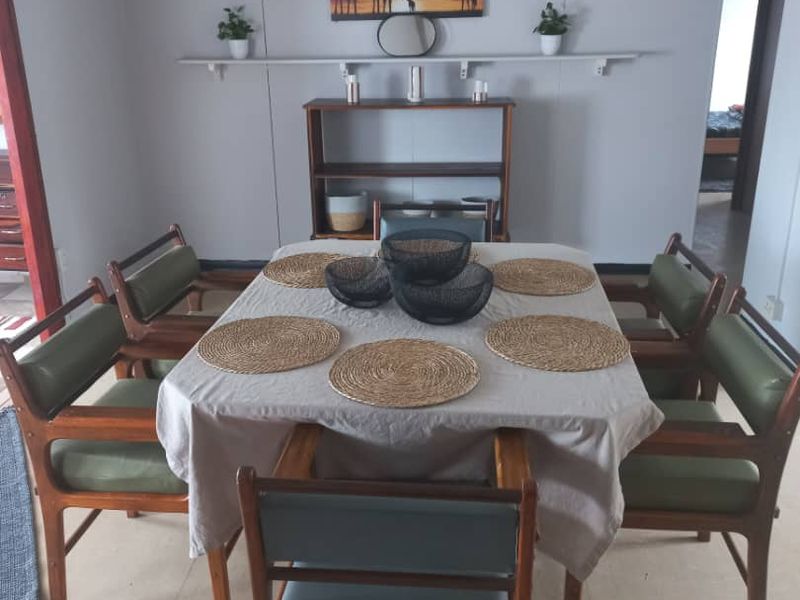 A dining room featuring a central dining area with an exposed ceiling beam and a wall-mounted display shelf.