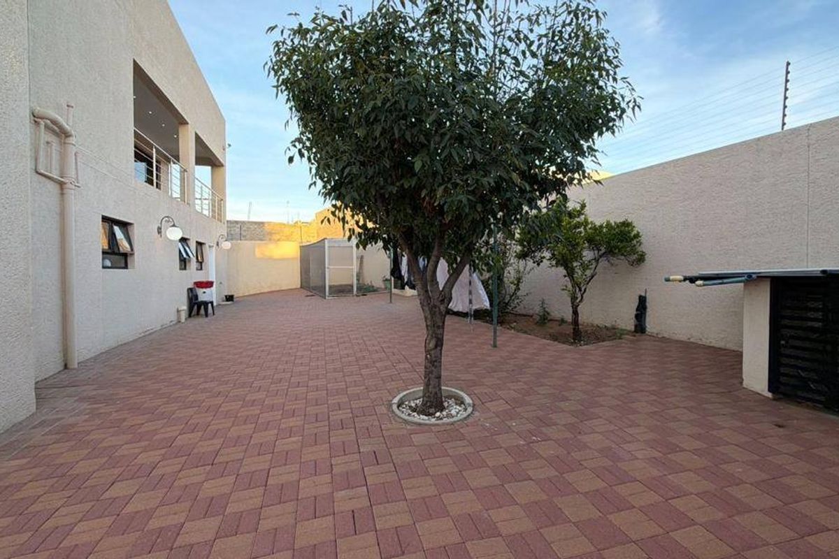 A spacious paved rear courtyard area featuring perimeter boundary walls, established trees, and direct access to the main dwelling.