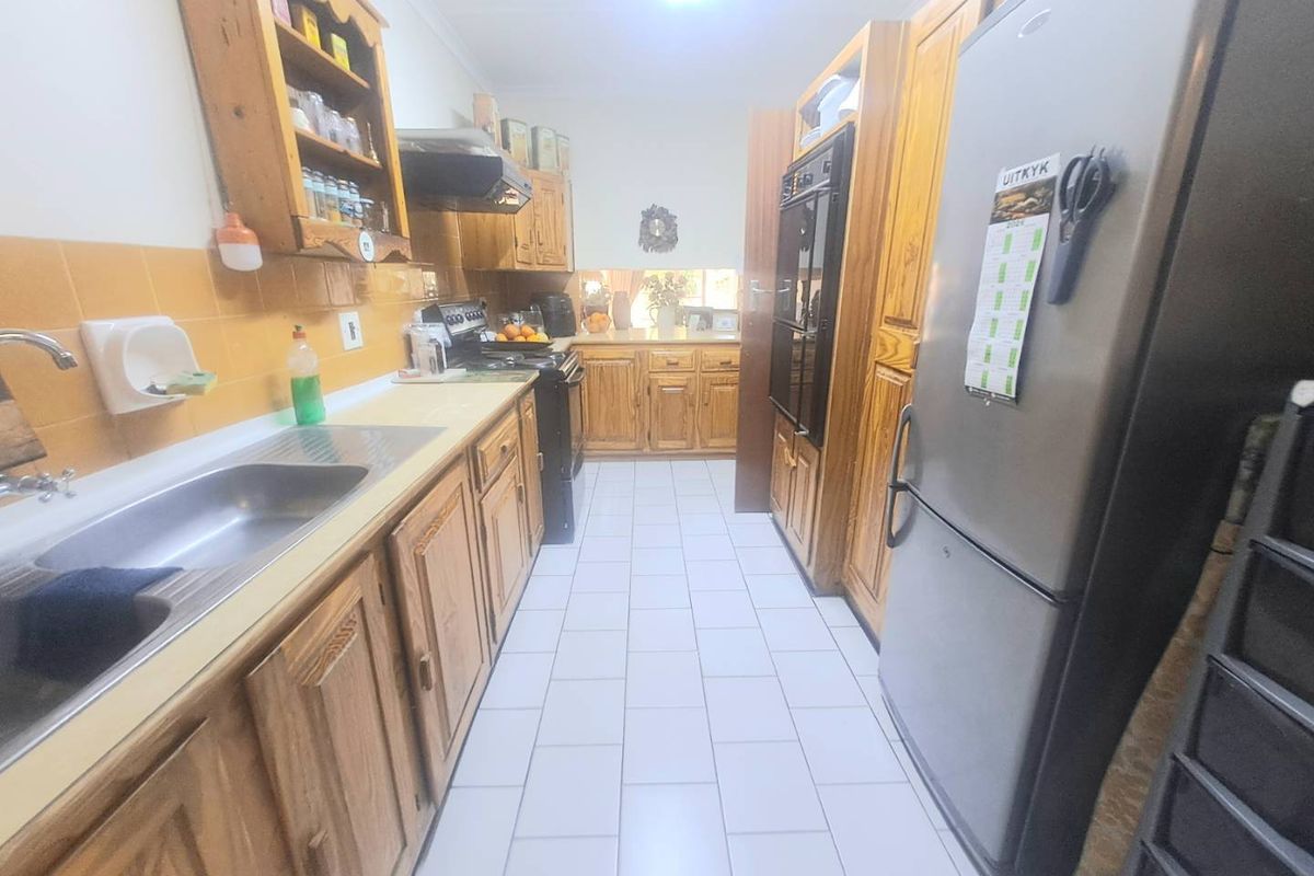 A functional galley-style kitchen featuring traditional wooden cabinetry, tiled backsplash, built-in oven, and tiled flooring, offering a classic layout with ample storage space.