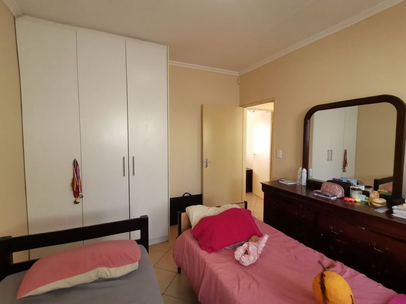 A bedroom featuring built-in wardrobes, tiled flooring, and neutral wall finishes, providing a functional space with direct access to an adjoining room.