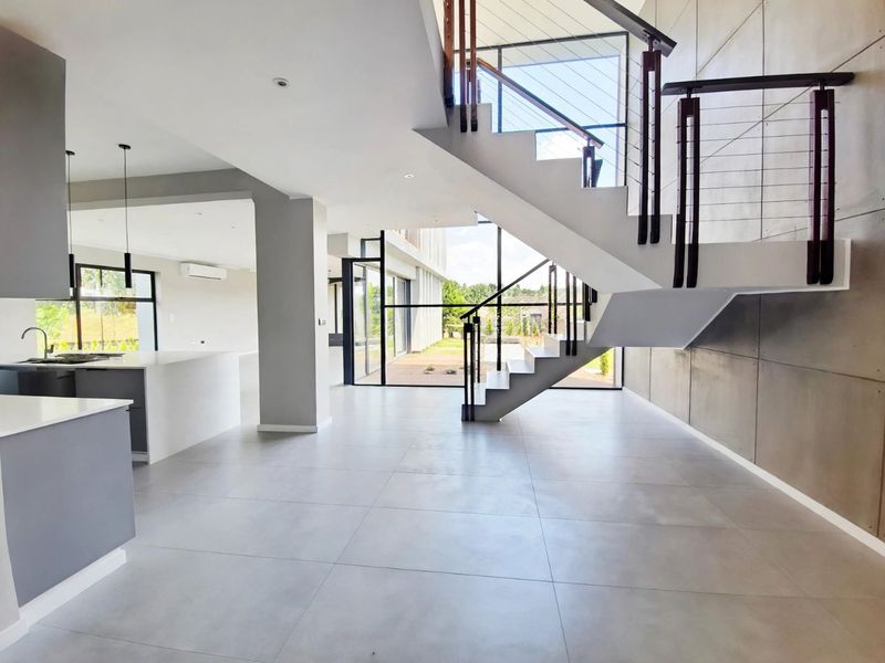 Spacious open-plan living area featuring a modern kitchen, large format floor tiles, a striking concrete feature wall, and a contemporary staircase.