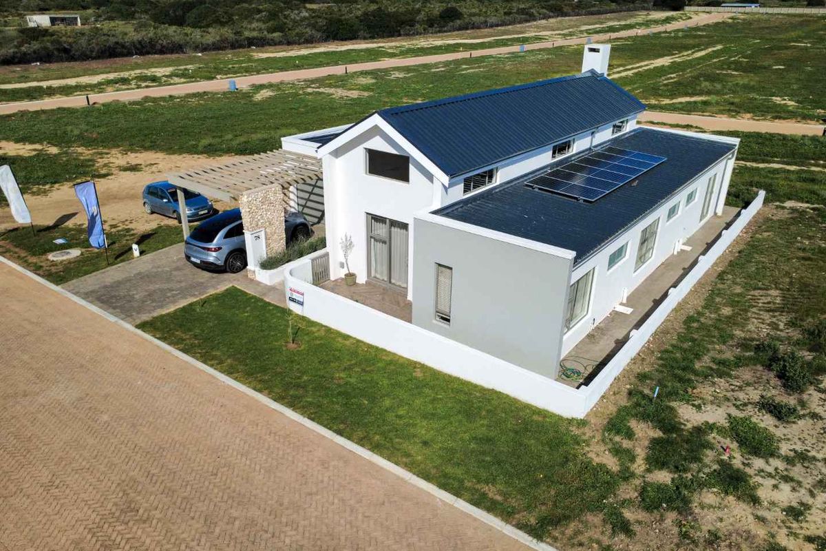 Aerial view of a modern single-story house featuring a metal roof, solar panels, a pergola-covered carport, and a perimeter boundary wall.