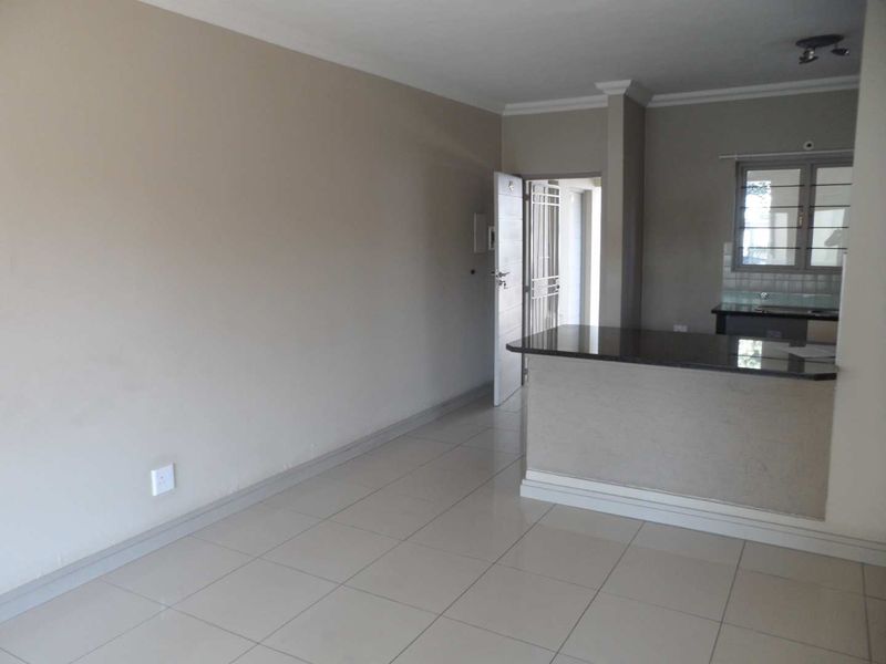 An open-plan living area featuring tiled floors, a breakfast bar with granite countertops, and a secure entrance door.
