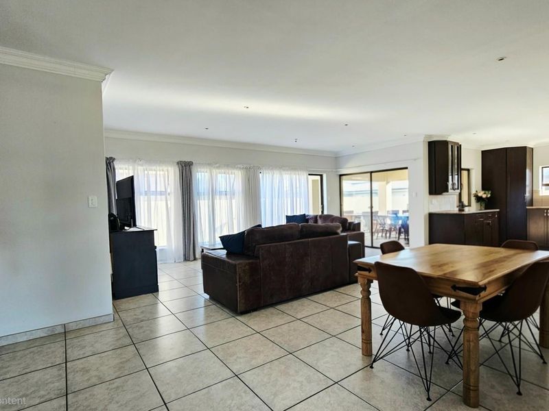 Spacious open-plan living and dining area featuring neutral tiled flooring, recessed lighting, and seamless flow to the outdoor patio through sliding glass doors.