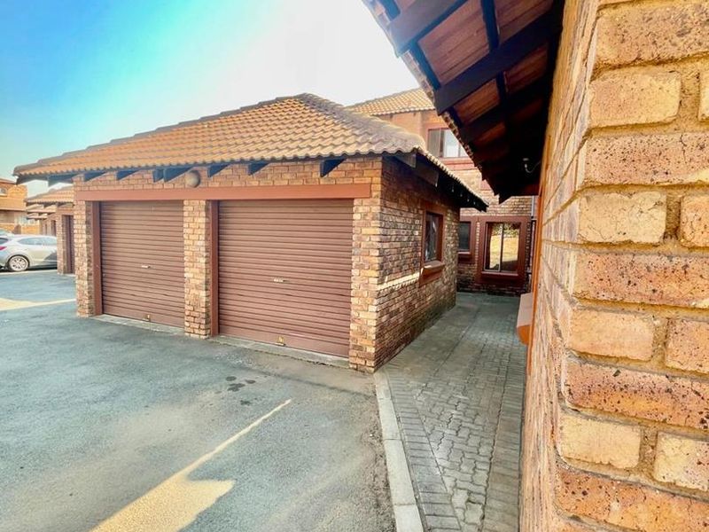 A view of a double garage with face brick exterior, tiled roof, and roller doors, situated within a paved cluster complex driveway.