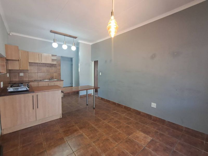 Open-plan kitchen and living area featuring tiled flooring, built-in wooden cabinetry, a gas hob, and a breakfast bar, offering a functional blank canvas.