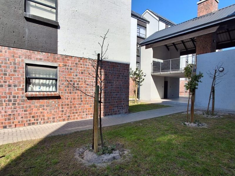 A view of the apartment complex exterior featuring brick and rendered facades, paved walkways, and a covered balcony area.