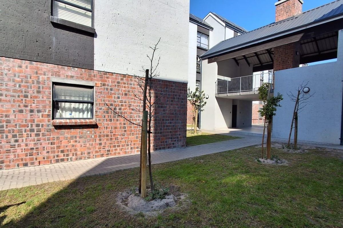 A view of the apartment complex exterior featuring brick and rendered facades, paved walkways, and a covered balcony area.