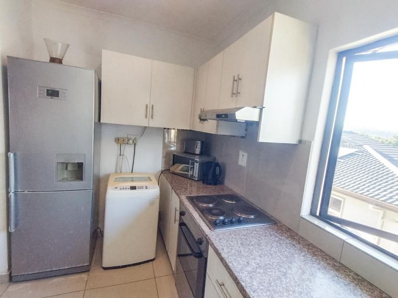 Compact kitchen featuring white cabinetry, laminate countertops, built-in oven, electric hob, and an extractor fan, with tiled flooring and natural light.