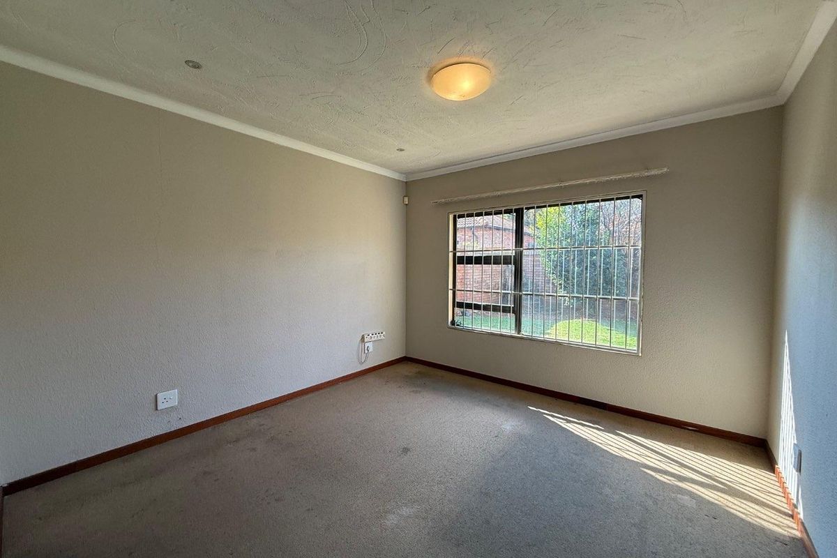 A vacant bedroom featuring neutral walls, fitted carpeting, and a window secured with metal burglar bars.
